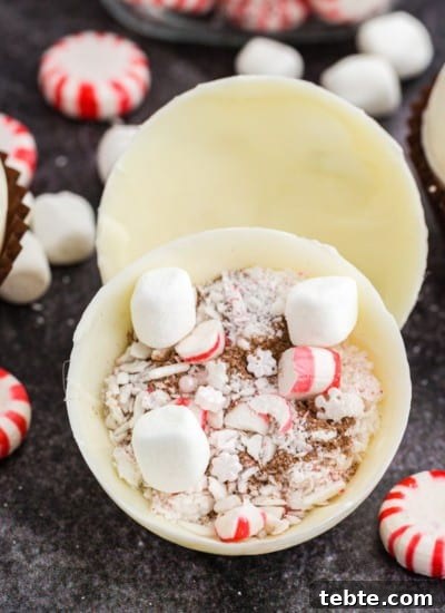 Peppermint hot chocolate bombs with hot chocolate, crushed candy canes, and mini marshmallows, on a dark marble countertop.