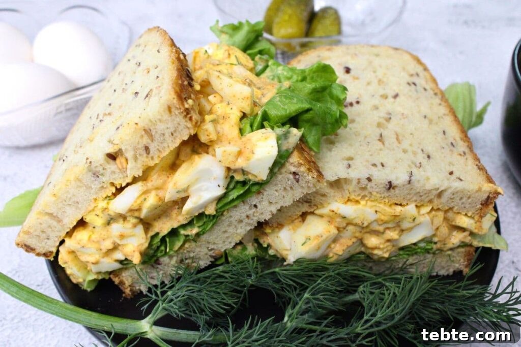 two halves of an air fryer egg salad sandwich on a black plate with fresh dill