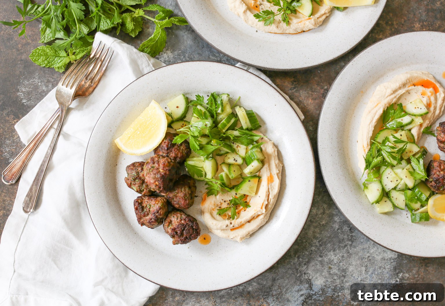 Spiced Lamb Kofta Recipe — Authentic Middle Eastern Meatballs 10 Overhead view of plated lamb kofta with hummus, cucumber salad, and lemon with napkins and forks.