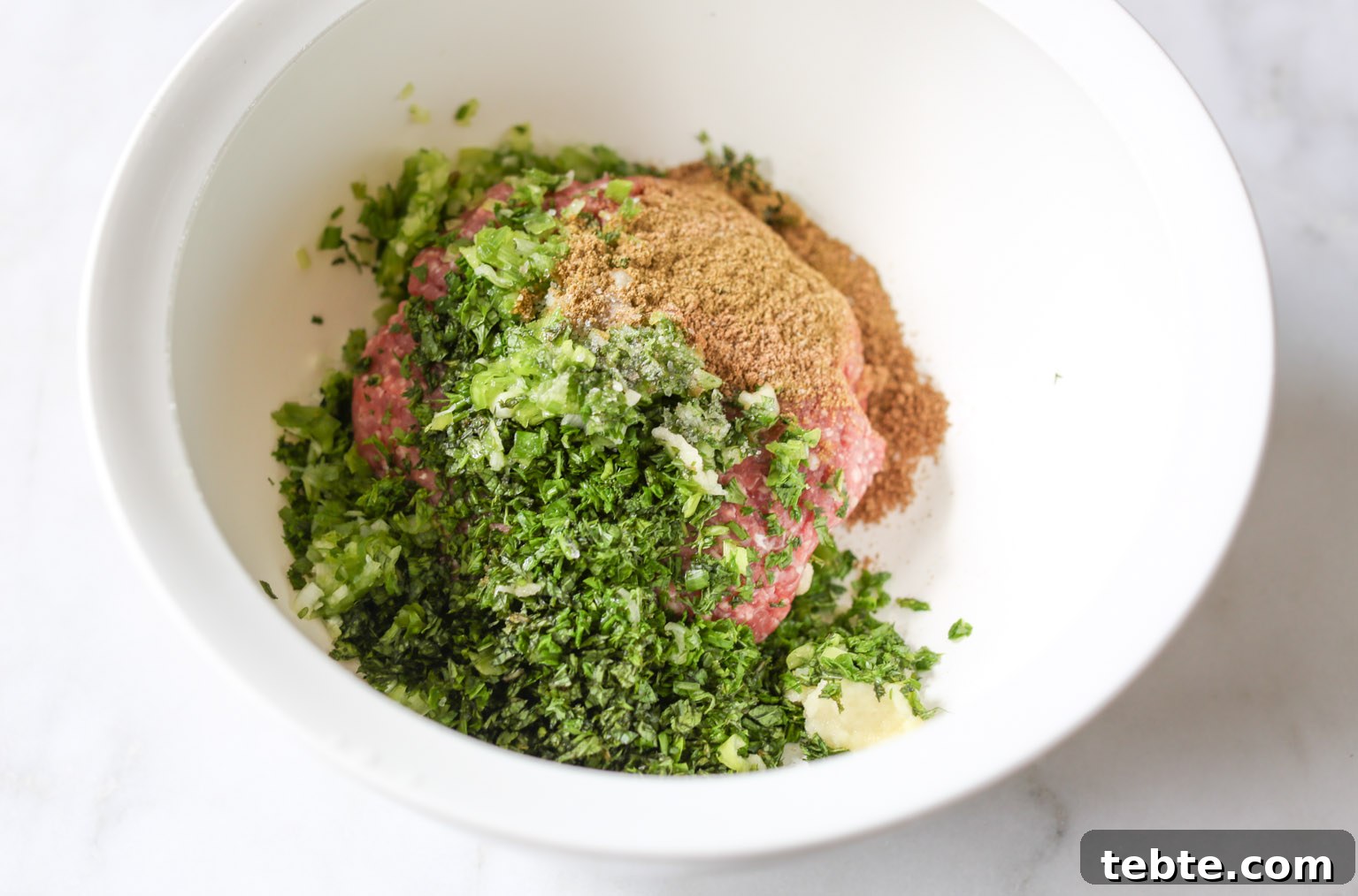 Overhead view of a mixing bowl with ingredients for spiced lamb meatballs. 