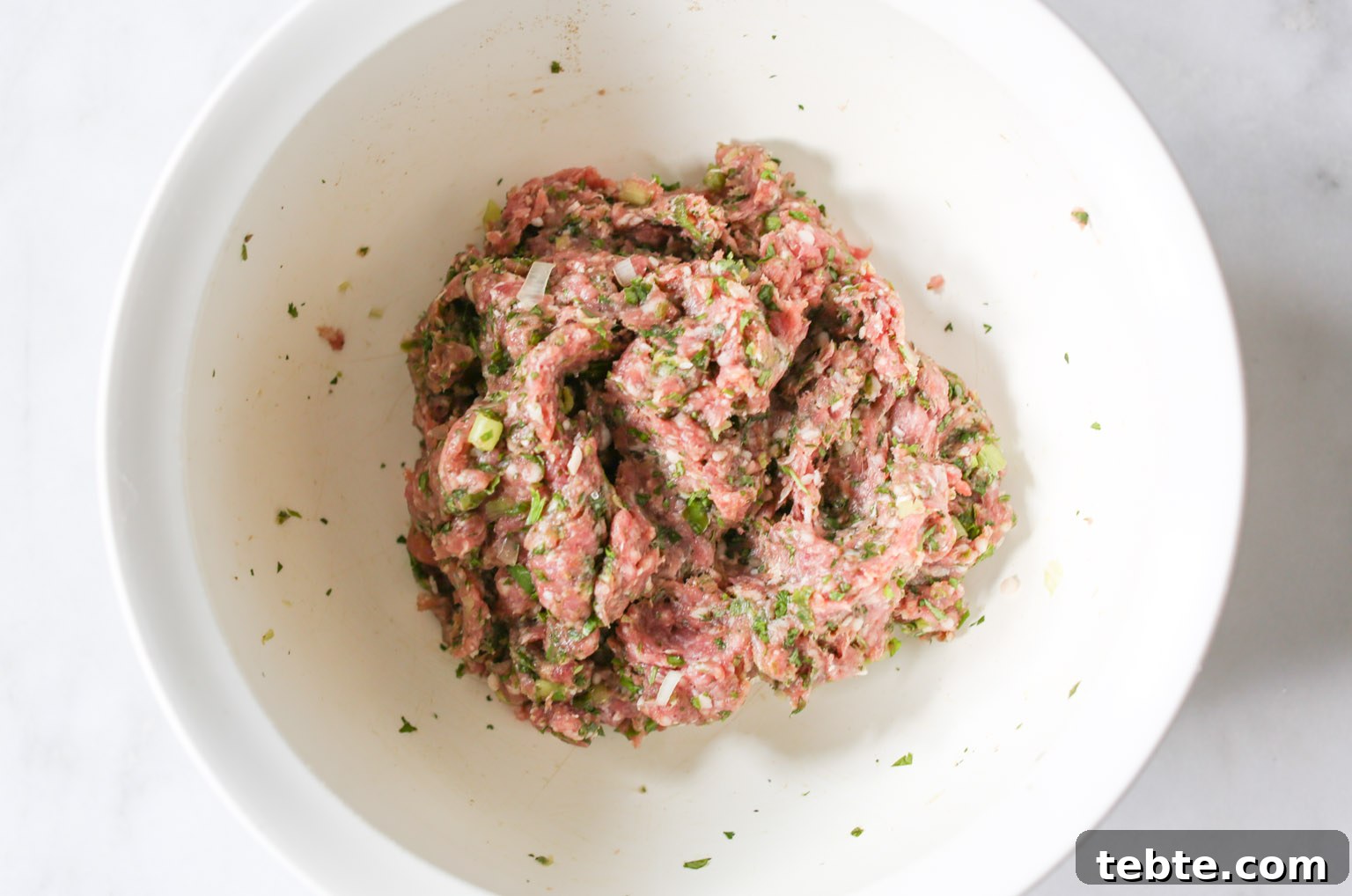 Overhead shots of all ingredients for spiced lamb meatballs mixed together and ready to be rolled into meatballs.