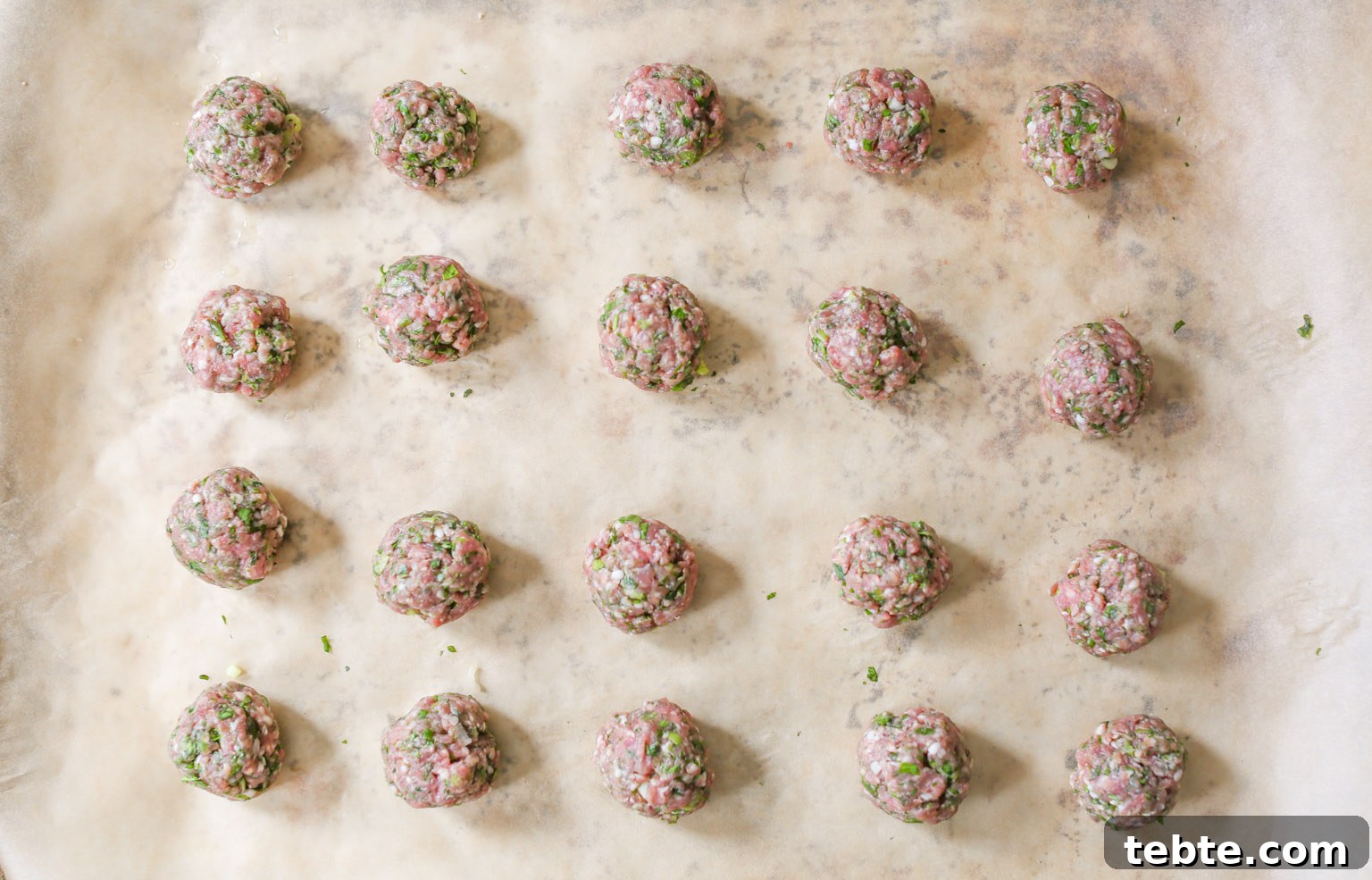 Rolled spiced lamb meatballs on a parchment-lined baking sheet before going into the oven.