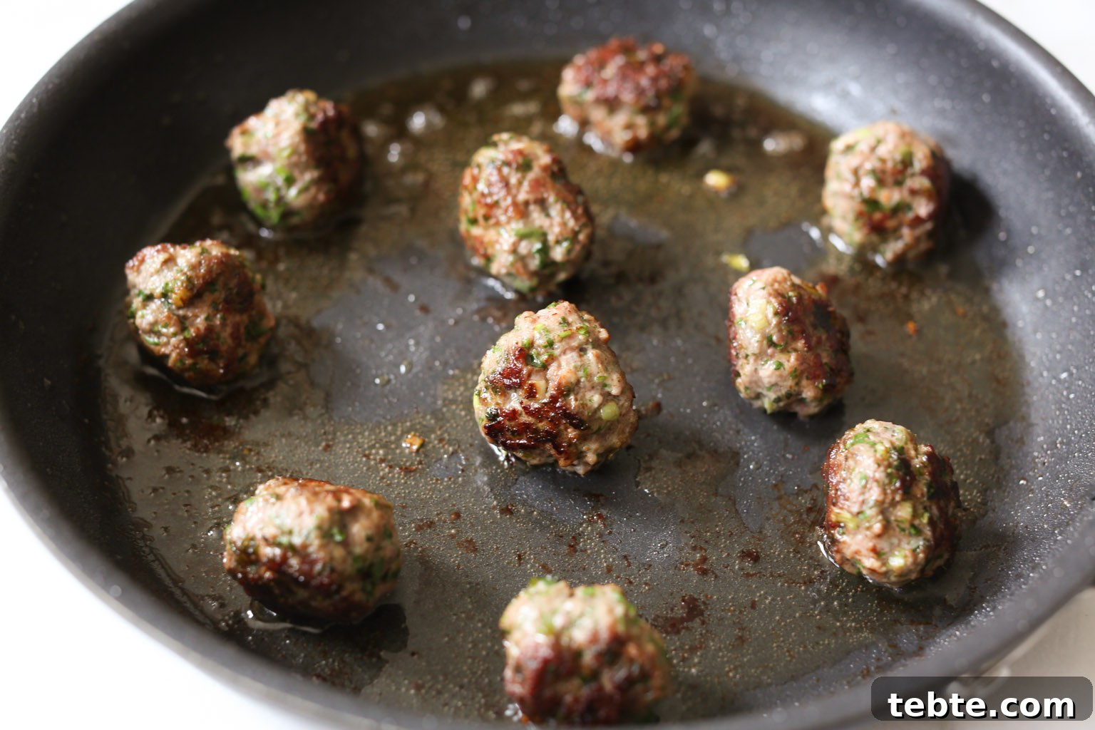 Spiced Lamb Kofta Recipe — Authentic Middle Eastern Meatballs 8 Lamb kofta being browned in oil in a skillet.