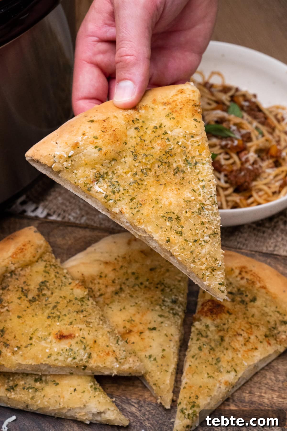 Crispy Garlic Pizza Bread Recipe — Cheesy Garlic Pull-Apart Loaf 2 Holding a slice of Garlic Pizza Bread over a bowl of spaghetti bolognese