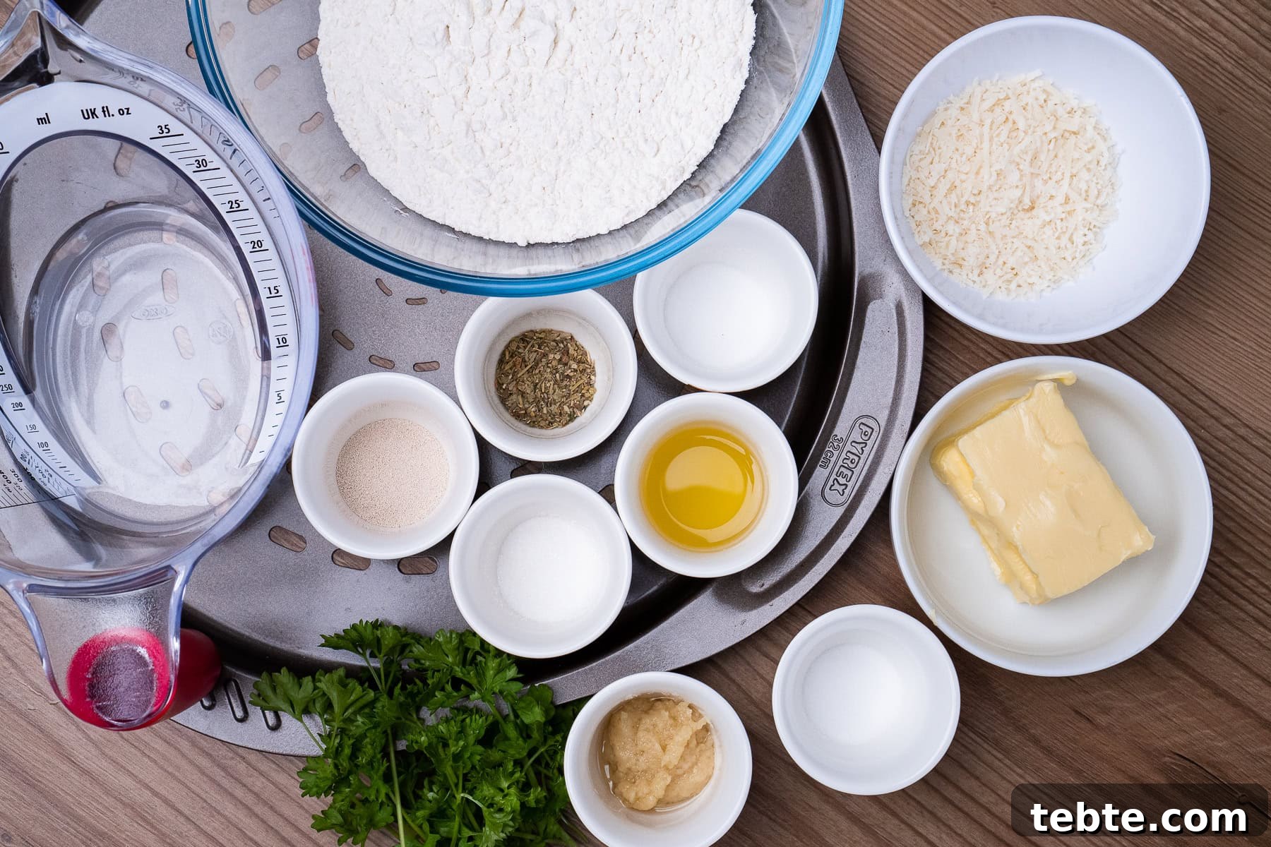 Crispy Garlic Pizza Bread Recipe — Cheesy Garlic Pull-Apart Loaf 17 Bowls of garlic,dried yeast,plain flour, mixed herbs, white sugar, unsalted butter, salt, warm water and grated parmesan cheese on a oven pizza tray