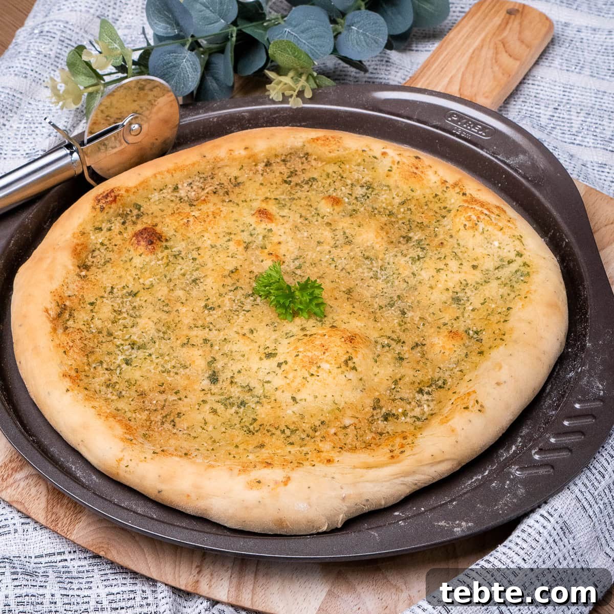 Crispy Garlic Pizza Bread Recipe — Cheesy Garlic Pull-Apart Loaf 33 Garlic Pizza Bread with fresh parsley leaves on top served on a round pizza tray ontop of a wooden pizza board with a pizza cutter on the side