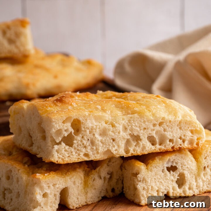 Slices of focaccia bread on a wooden plate showing off the airy dough.