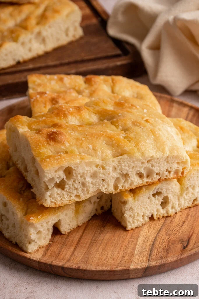 Authentic Italian Focaccia Bread Recipe 3 Sliced focaccia bread layered on a wooden plate.