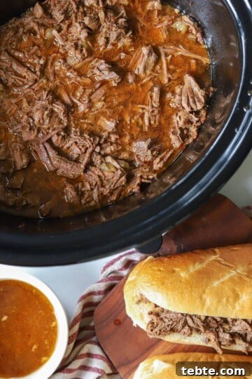 Slow Cooker beef in crockpot with sandwiches on the side.