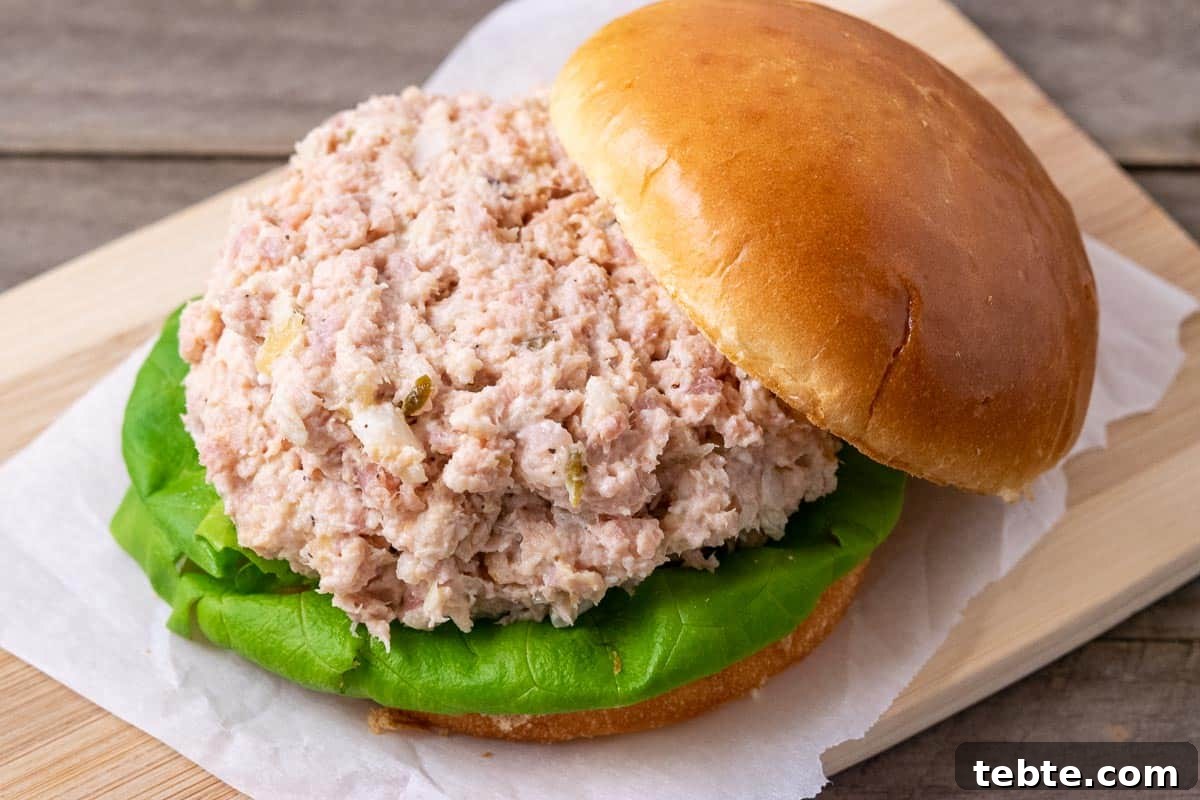 Classic Ham Salad Sandwich Recipe for Quick Lunch Ideas 5 a sandwich roll bottom filled with lettuce and ham salad spread and the sandwich roll bun top resting on the edge of it