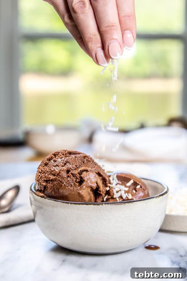 Creamy Dairy-Free Chocolate Ice Cream Recipe 2 A scoop of ice cream in a bowl with a hand sprinkling coconut on top