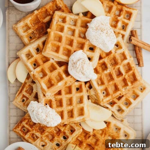 A stack of waffles with slices of apples and whipped cream.
