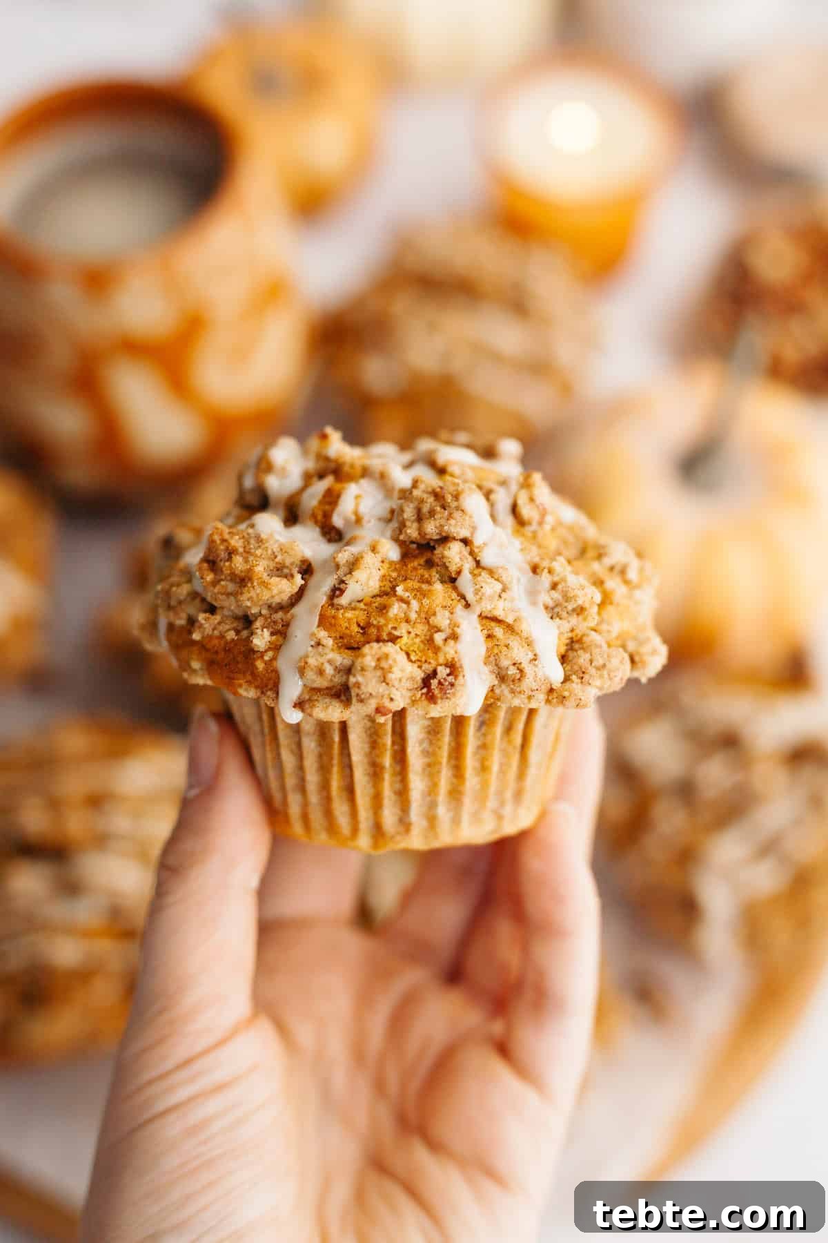 Pumpkin Pecan Muffins with Crunchy Pecan Streusel 8 A hand holding a pecan pumpkin muffin with a white glaze.