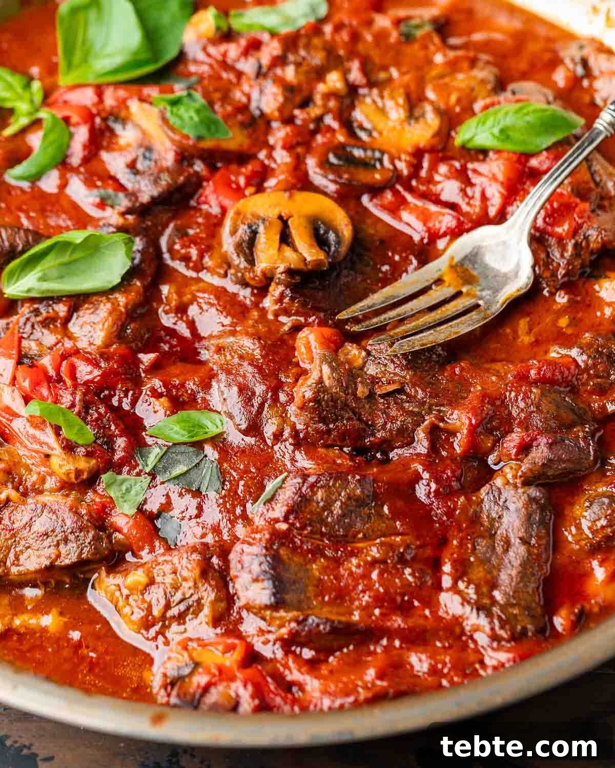 Steak Pizzaiola Recipe: Flavorful Affordable Weeknight Steak Dinner 2 Steak pizzaiola in pan with large fork and basil leaves.