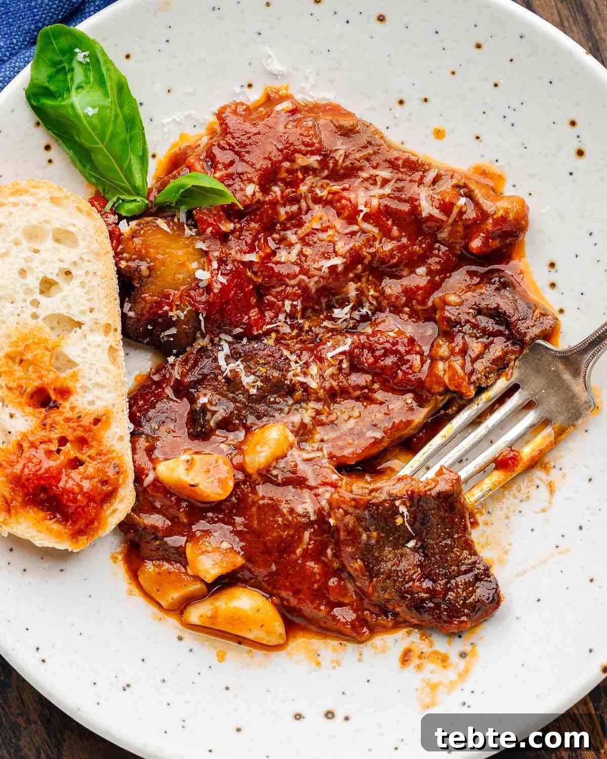 Steak Pizzaiola Recipe: Flavorful Affordable Weeknight Steak Dinner 3 White plate with cut piece of steak pizzaiola and lots of garlic cloves.