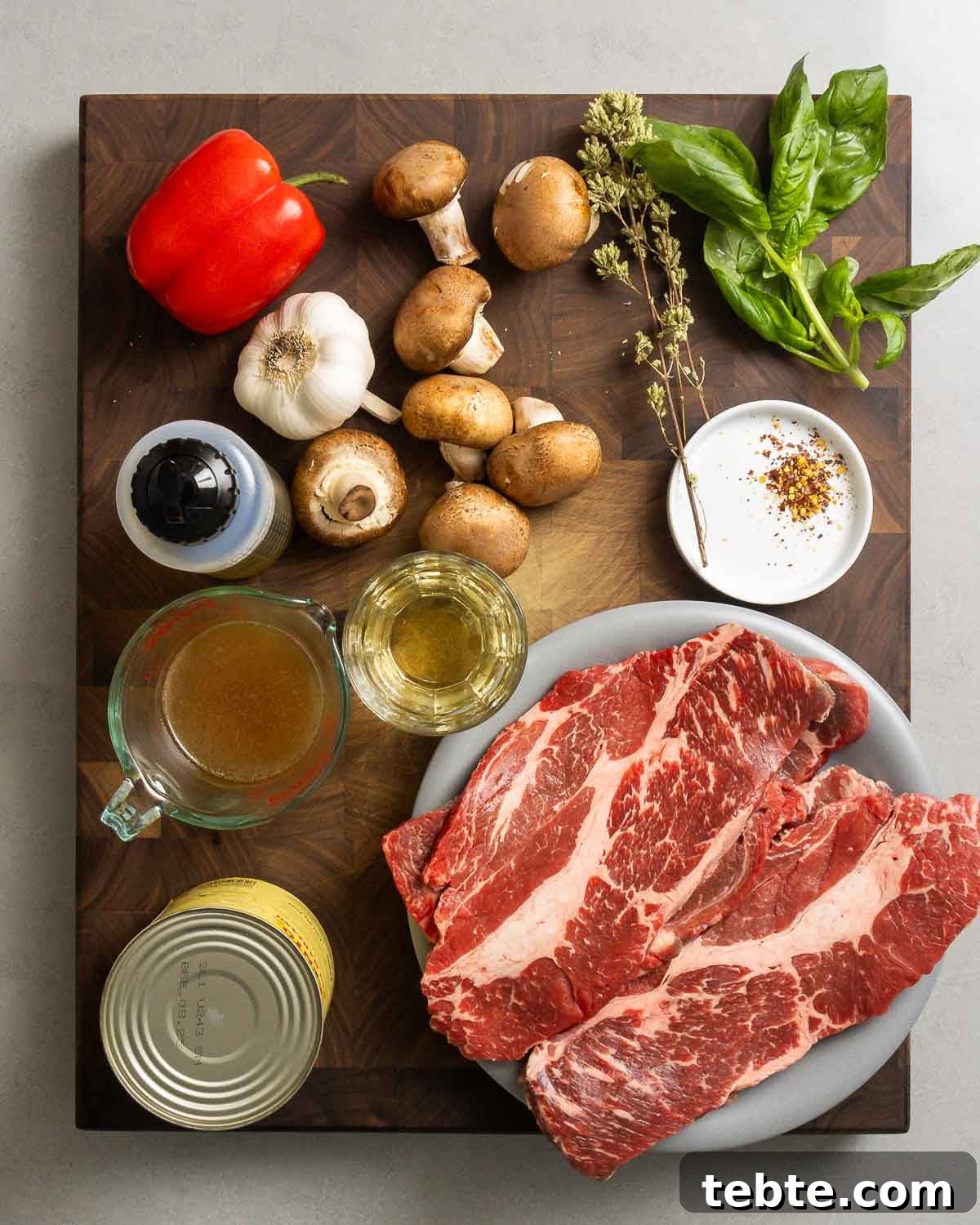 Steak Pizzaiola Recipe: Flavorful Affordable Weeknight Steak Dinner 4 Ingredients shown: stuck cheaks, red bell pepper, mushrooms, oregano, basil, garlic, olive oil, beef stock, white wine, red pepper flakes, and plum tomatoes.