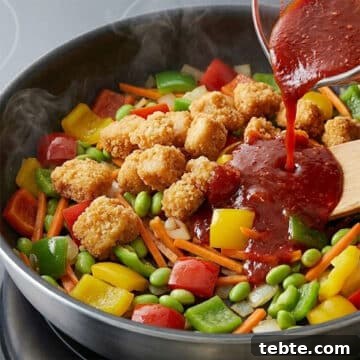 Breaded chicken and sauce being added on top of the veggies in nonstick pan. 