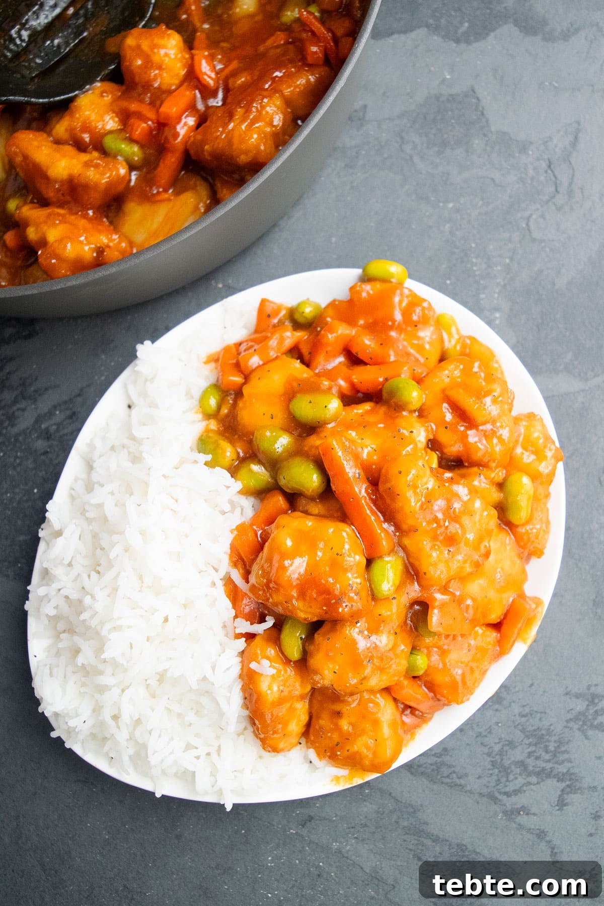 Asian chicken with veggies and sauce served in white dish with steamed rice. 