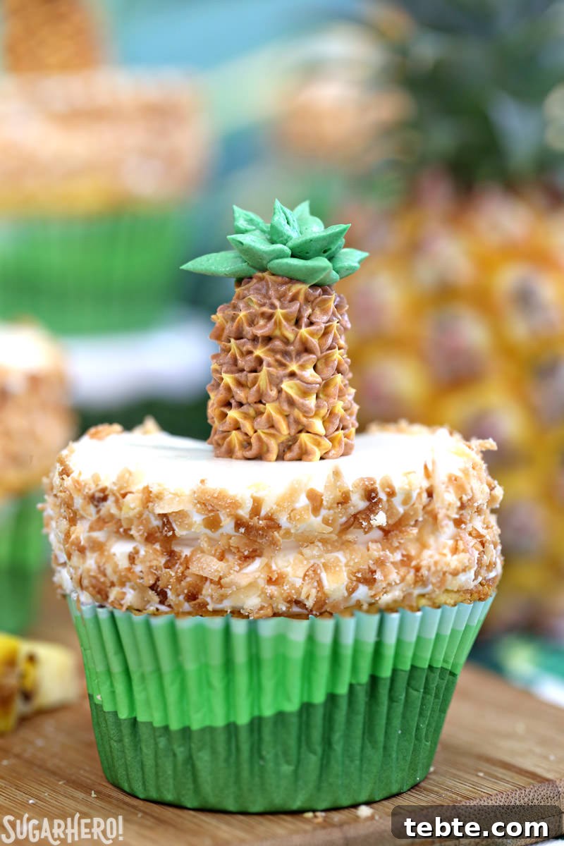 Close-up of a single pineapple cupcake with coconut frosting and a buttercream pineapple on top | From SugarHero.com