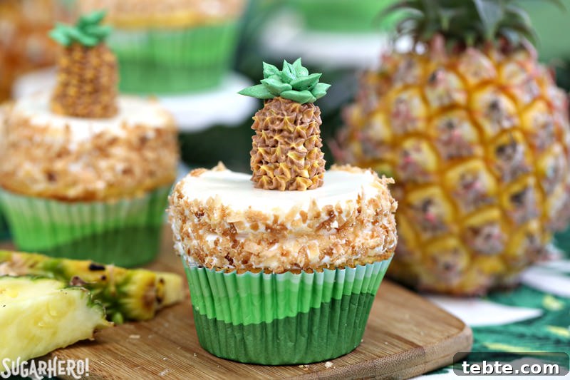 Two pineapple cupcakes with coconut buttercream and fresh pineapple pieces | From SugarHero.com