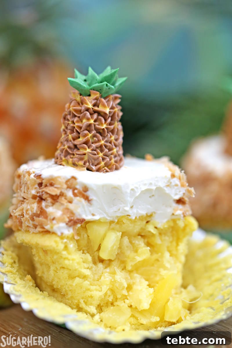 Pineapple cupcake with a bite taken out of it and fresh pineapple in the middle, topped with coconut buttercream | From SugarHero.com