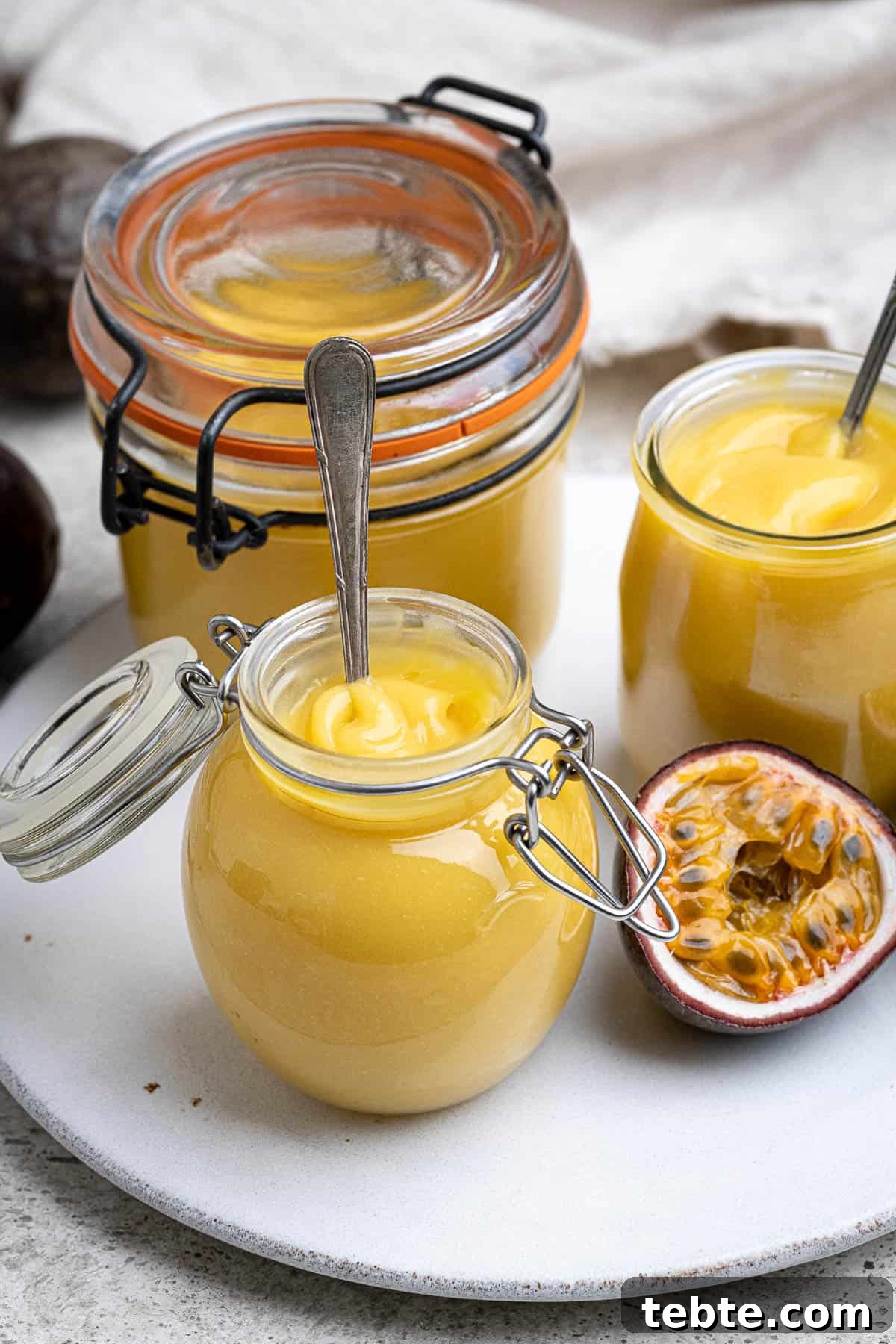 Vibrant Vegan Passion Fruit Curd Recipe for Tarts & Toast 2 Three jars of vegan passion fruit curd on a plate with a halved passion fruit.