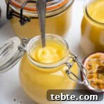 Vibrant Vegan Passion Fruit Curd Recipe for Tarts & Toast 11 Close up of a small jar of vegan passion fruit curd with a spoon in it.