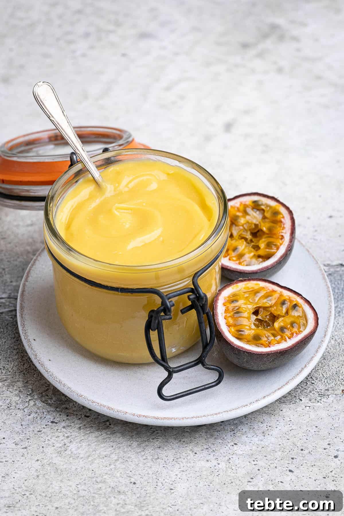 Vibrant Vegan Passion Fruit Curd Recipe for Tarts & Toast 9 A jar of vegan passion fruit curd on a plate with a halved passion fruit.