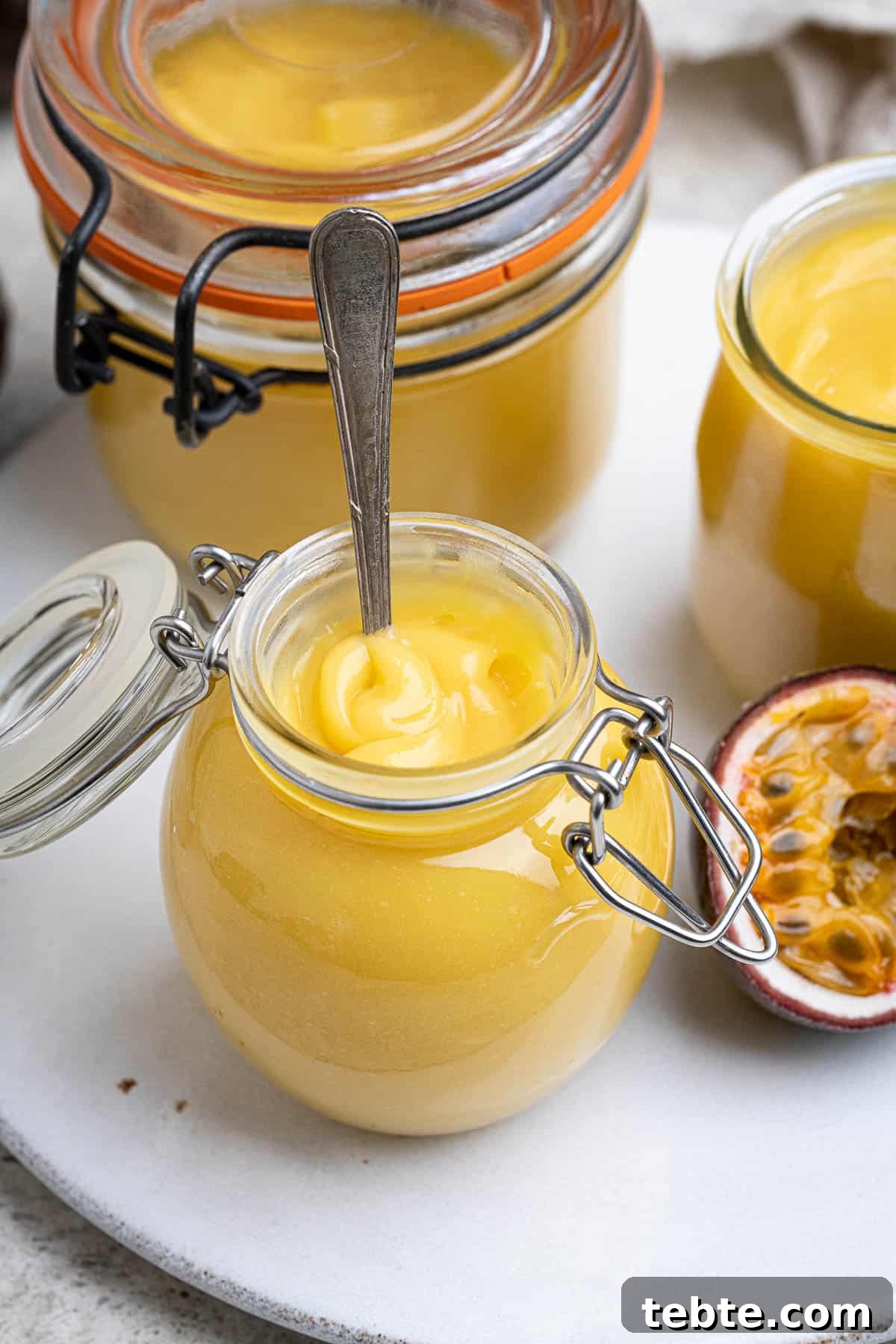 Vibrant Vegan Passion Fruit Curd Recipe for Tarts & Toast 10 Close up of a small jar of vegan passion fruit curd with a spoon in it.