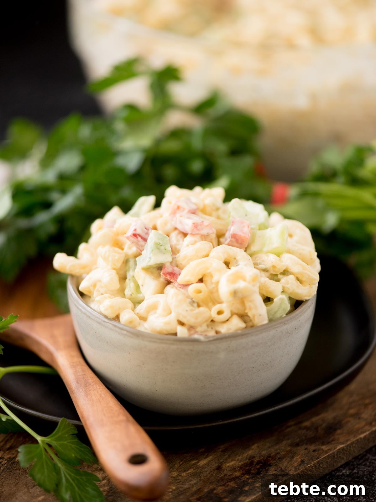 Grandma’s Old-Fashioned Macaroni Salad Recipe – Classic Comfort Food 2 Macaroni salad in a grey bowl surrounded by a serving spoon and fresh parsley.