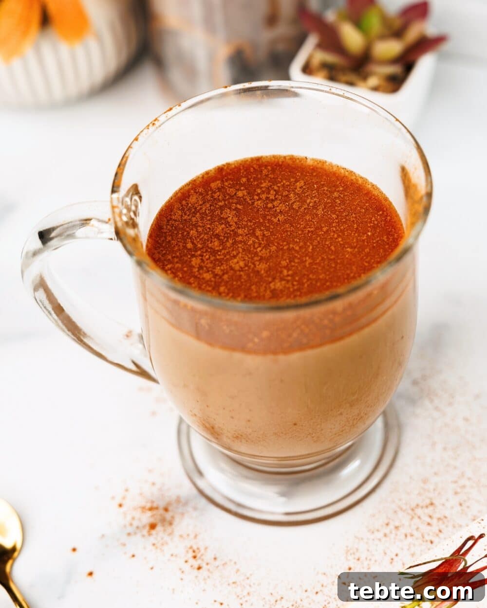 Close-up of chai latte in a clear mug with a cinnamon topping and scattered cinnamon on the table.
