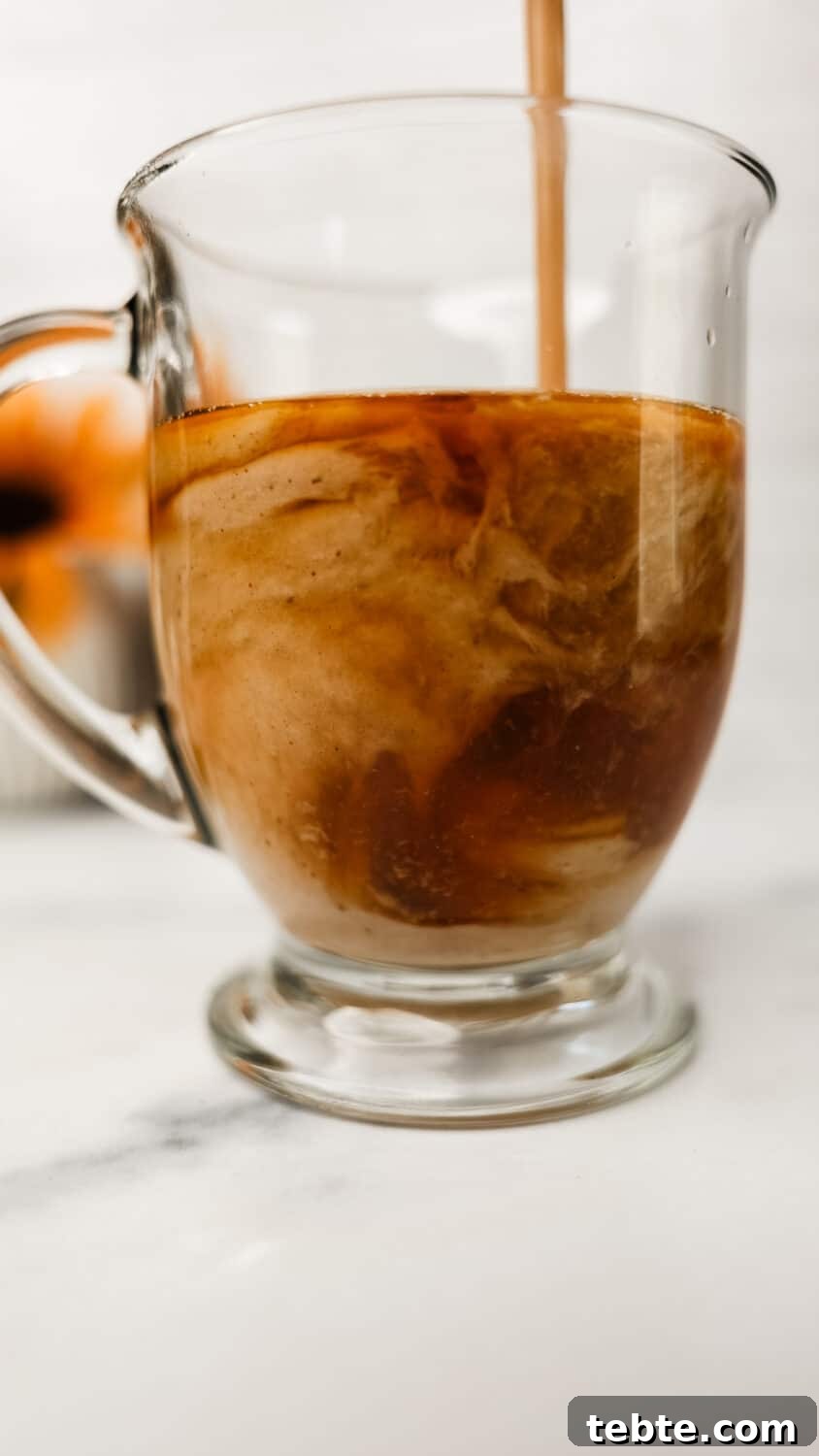 Protein chai latte being poured into a clear mug, swirling with tea.