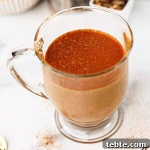 Close-up of chai latte in a clear mug with a cinnamon topping and scattered cinnamon on the table.