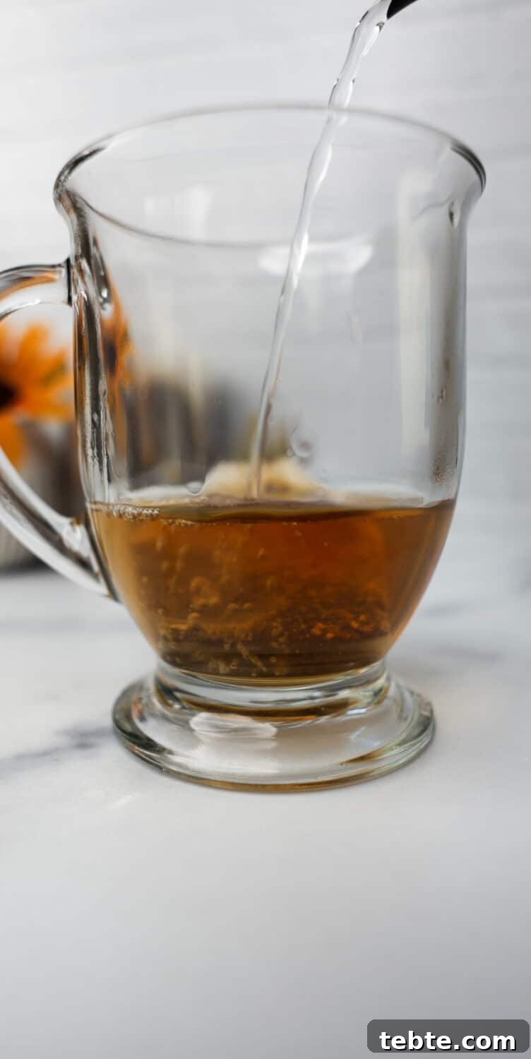 Hot water being poured into a glass mug with chai tea bag steeping.