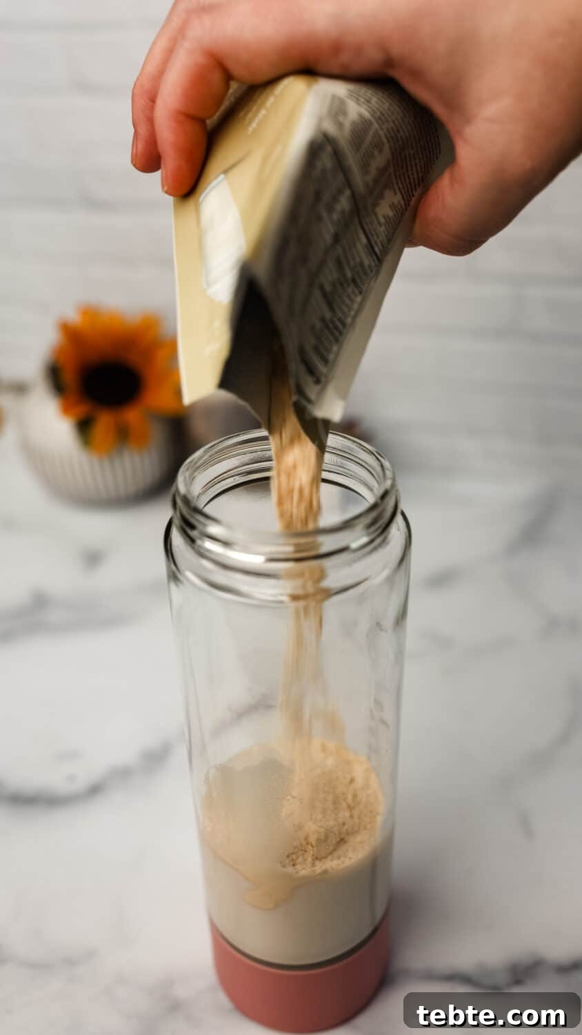 Protein powder being poured from a packet into a blender bottle with almond milk.