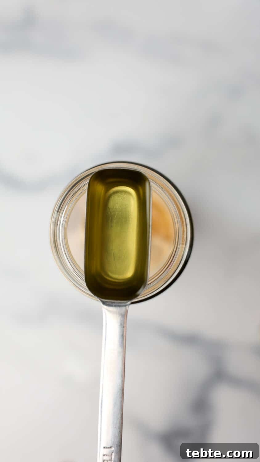 Measuring spoon with avocado oil held over a jar of protein powder.