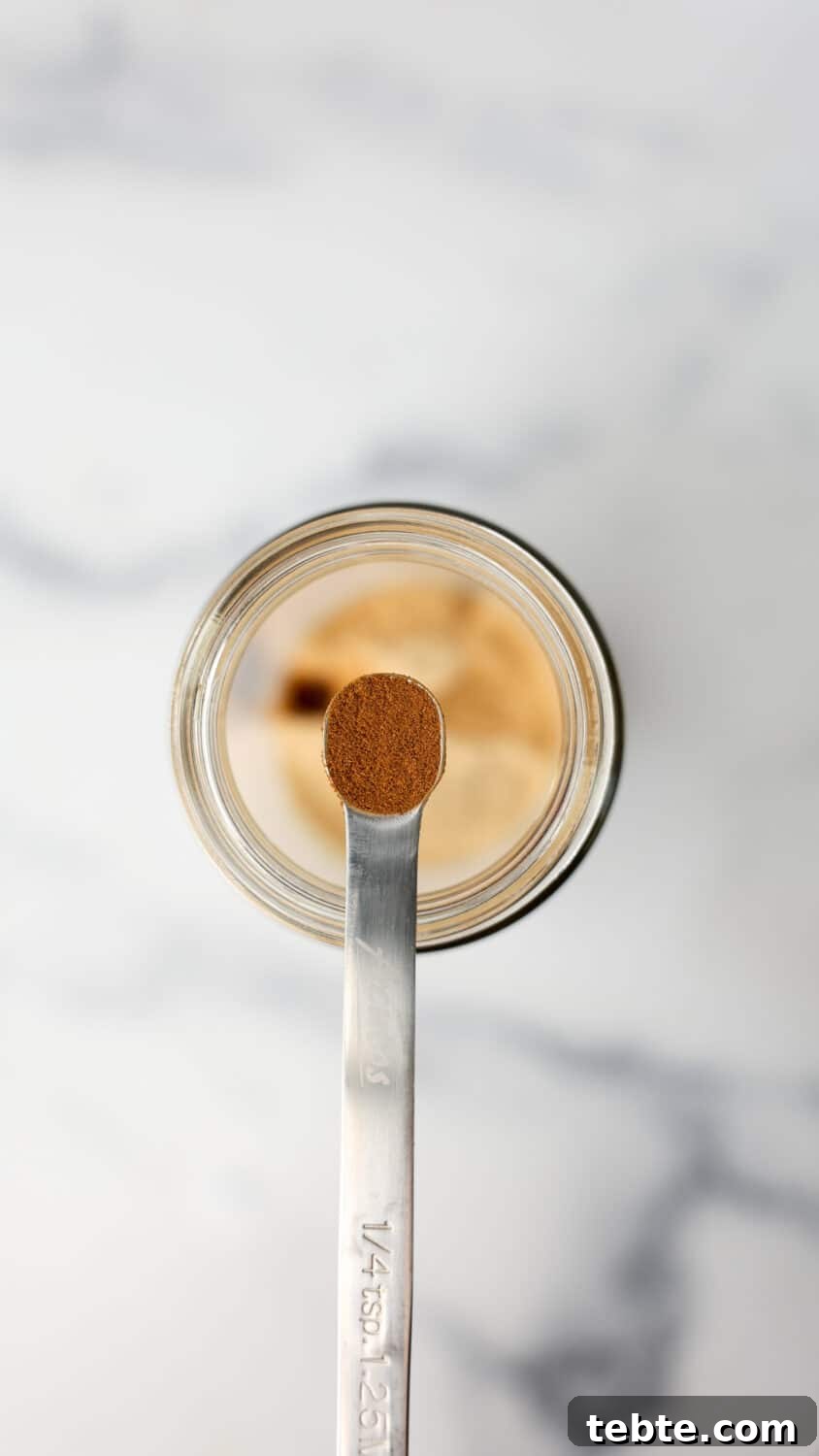Measuring spoon with ground chai spice held over a jar of protein powder.
