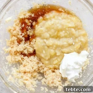 Ingredients combined in a glass bowl, possibly for baking, including mashed bananas, sugars, and a dollop of sour cream or yogurt.
