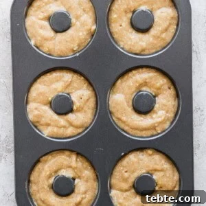 A six-cavity donut baking pan filled with raw donut batter, ready to be baked.