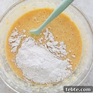 A glass bowl containing a mixture of flour and a liquid batter with a green silicone spatula.