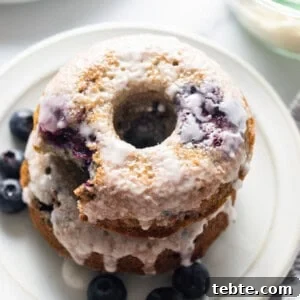 A stack of blueberry glazed donuts on a plate.