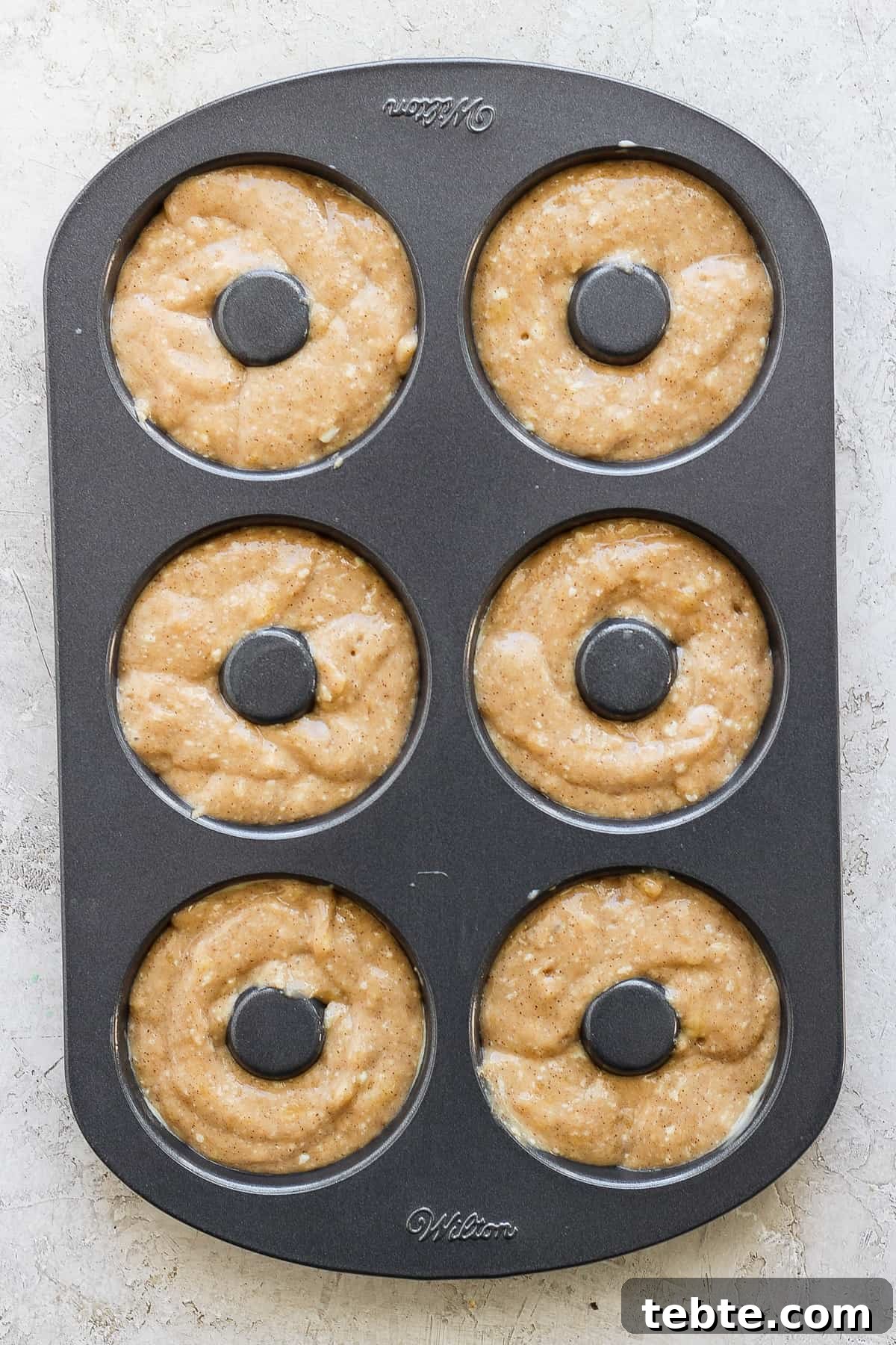 A six-cavity donut baking pan filled with raw donut batter, ready to be baked.