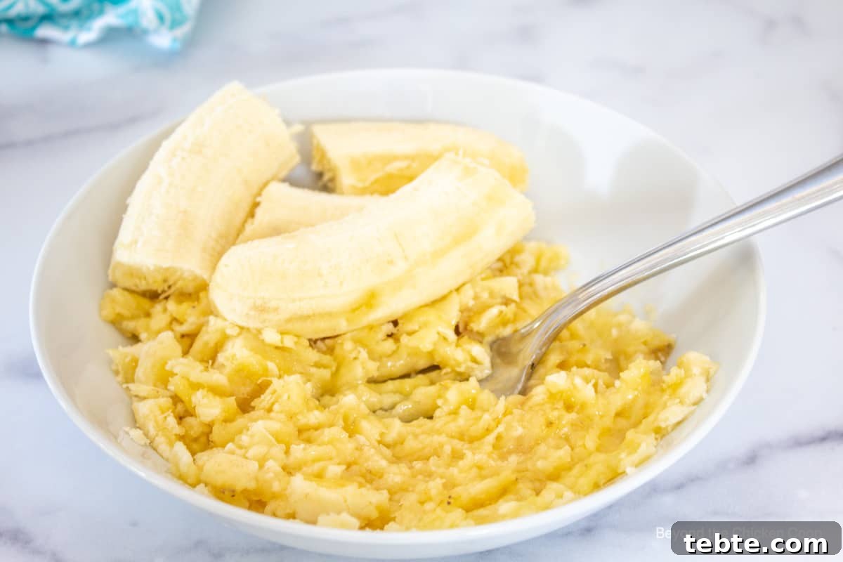 Mashed bananas with a fork in a white bowl.
