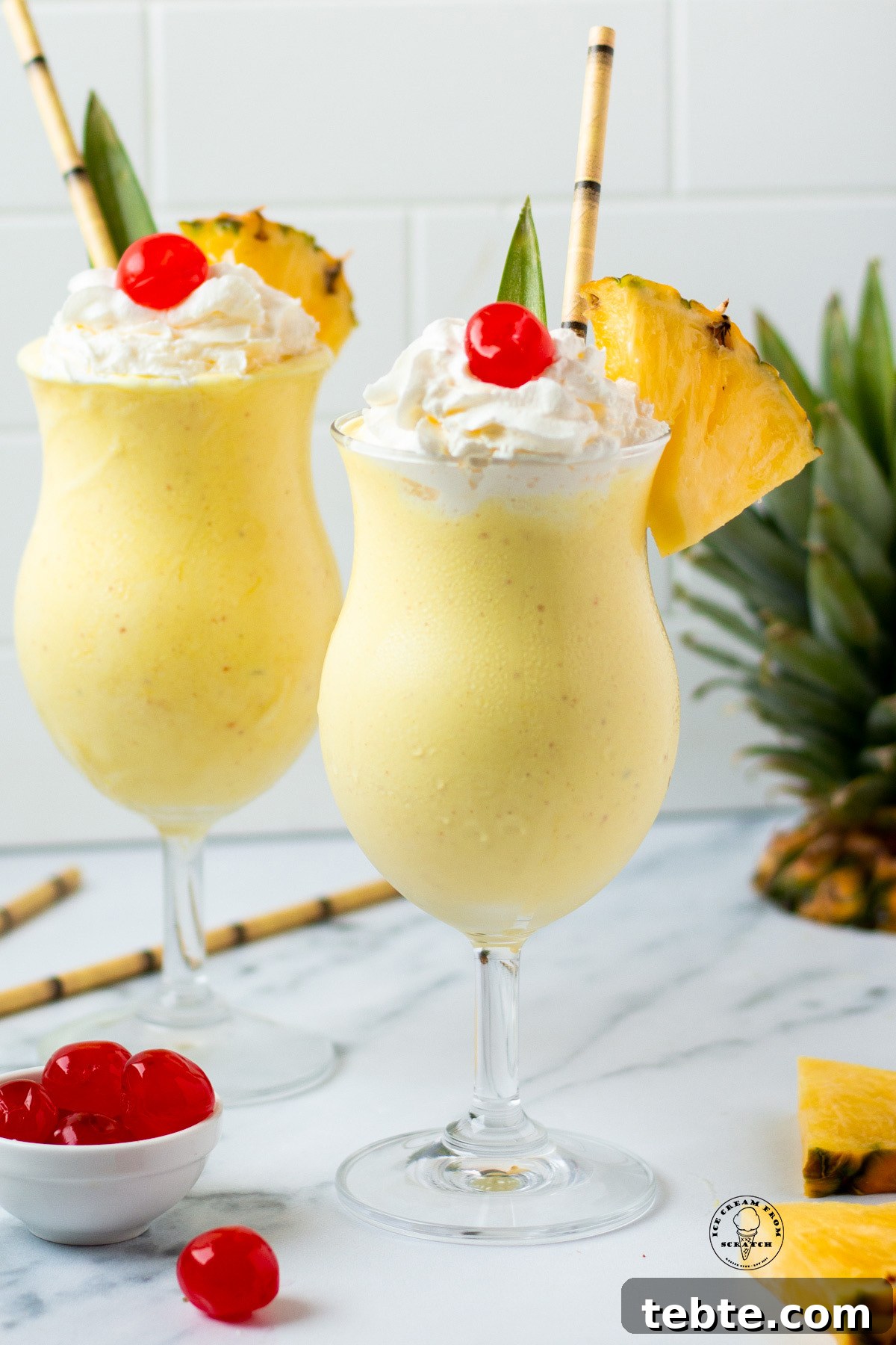Creamy Pineapple Milkshake Recipe – Tropical Smoothie Treat 2 Two pineapple milkshakes in hurricane glasses garnished with a pineapple leaf, whipped cream, cherries, and fresh pineapple wedges.