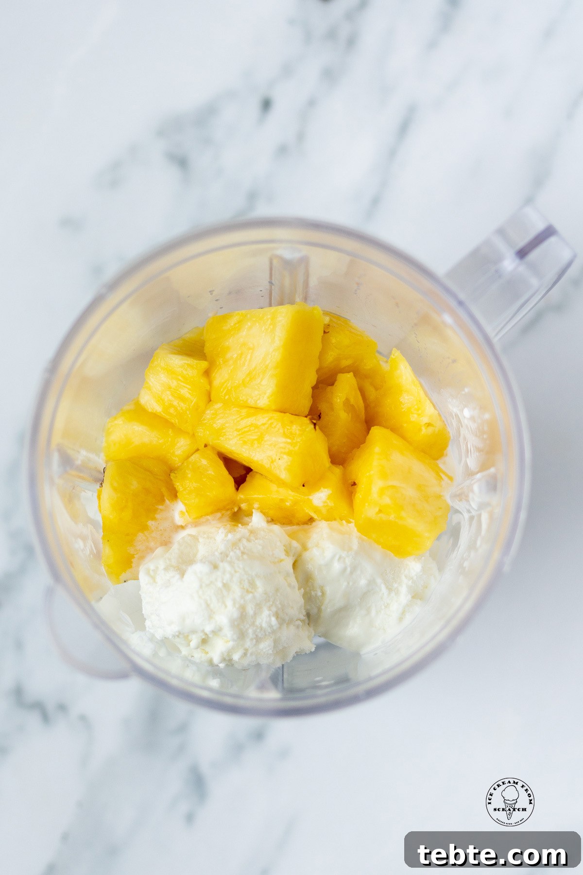 Creamy Pineapple Milkshake Recipe – Tropical Smoothie Treat 4 Pineapple pieces and vanilla ice cream in a blender, viewed from overhead