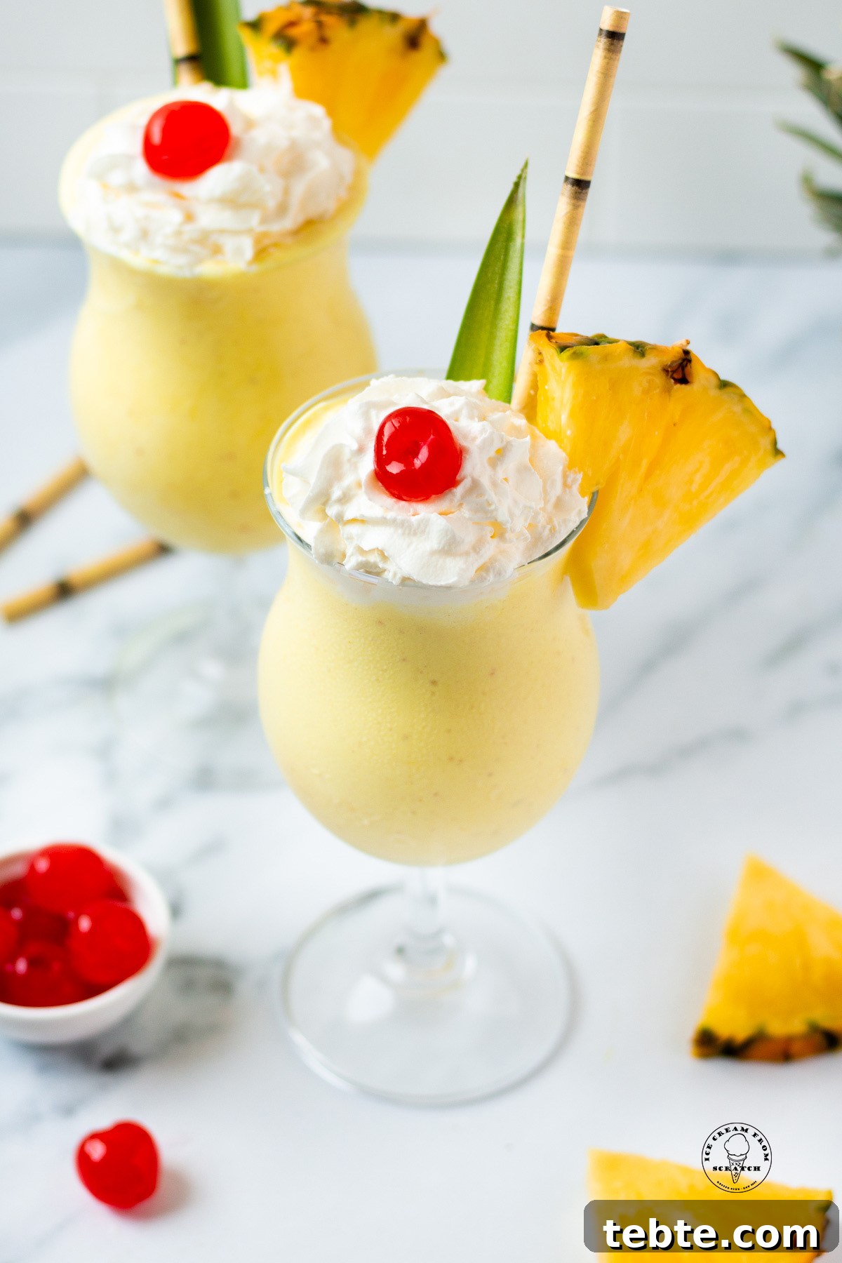 Creamy Pineapple Milkshake Recipe – Tropical Smoothie Treat 6 Looking down on two pineapple milkshakes garnished with cherries, pineapple slices, and bamboo straws