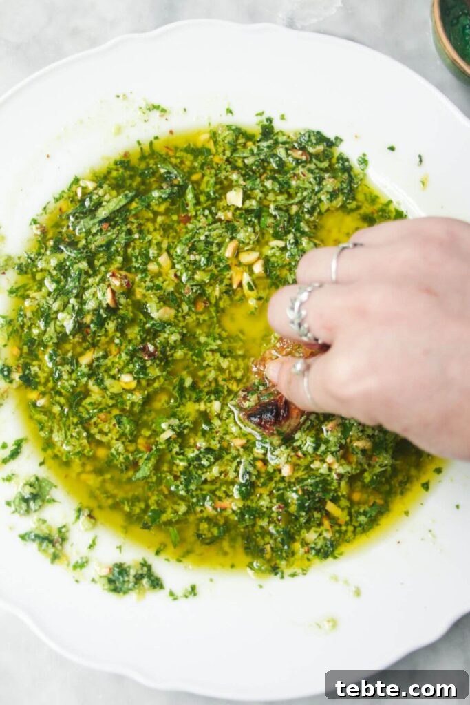 Jalapeño Popper Bread with Creamy Dipping Oil Recipe 9 A hand sweeping bread through pesto dipping oil in a scalloped white plate.