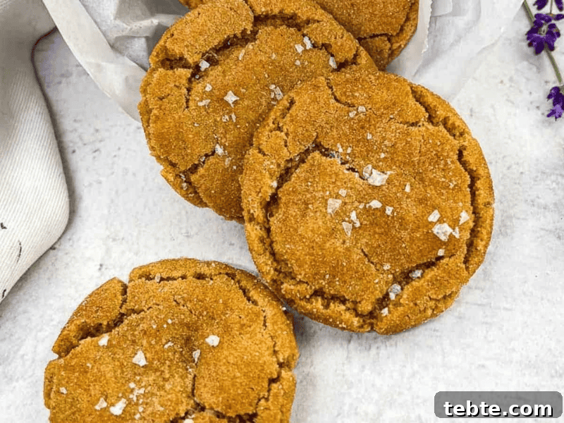 13 Christmas Cookies That Win Every Office Cookie Exchange 11 Three brown butter snickerdoodle cookies arranged on a white surface, sprinkled with sea salt flakes, with a white cloth and purple flowers on the side.