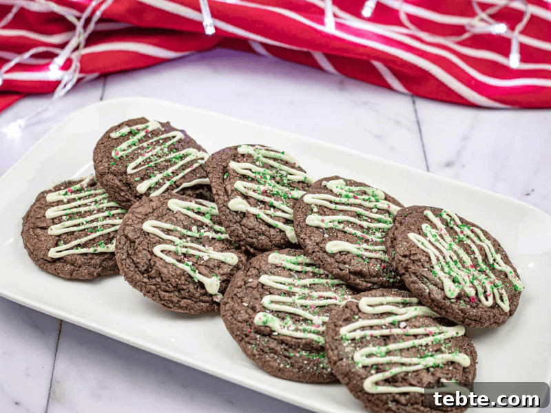 13 Christmas Cookies That Win Every Office Cookie Exchange 3 A plate of chocolate cookies topped with white icing and green sprinkles. A red and white striped cloth is in the background.