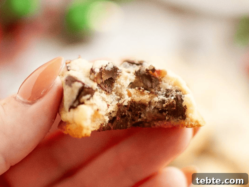 13 Christmas Cookies That Win Every Office Cookie Exchange 5 A hand holding a half-eaten chocolate chip cookie with visible chunks of chocolate and a blurred background.